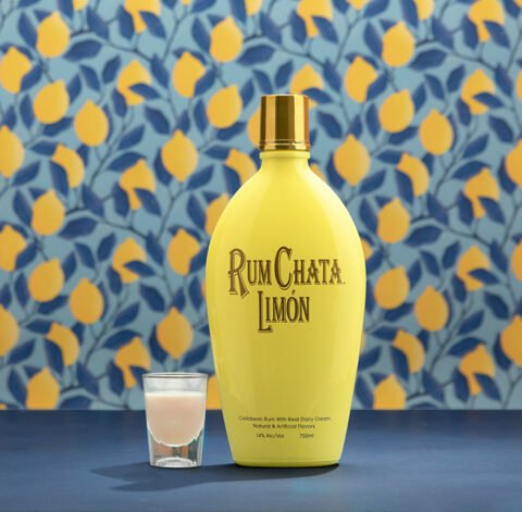 Un shooter de chata aux agrumes et une bouteille de rumchata limon devant un papier peint de citron et feuilles blueues