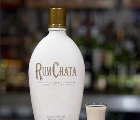 A shot of Irish chata and a bottle of Rumchata in front of a blurry wall of spirit bottles