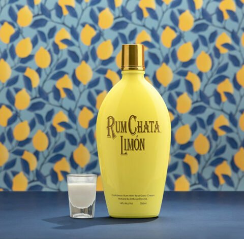 A shot of limon berry and a bottle of Rumchata Limon in front of a blue leaves and lemon wallpaper