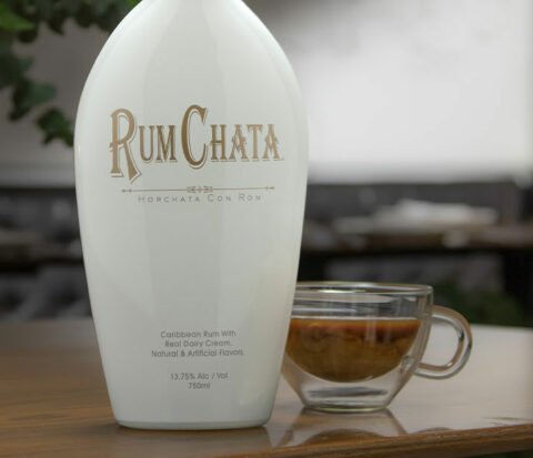 Une tasse en verre de cafe et rumchata avec une bouteille de rumchata sur une table en bois