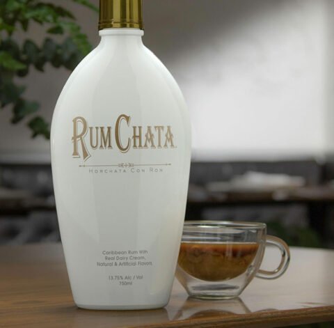 A glass cup of rumchata cacao nut brew and a bottle of Rumchata on a wooden table