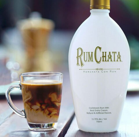 A glass cup of rumchata coconut coffee and a botlle of Rumchata on a picnic table