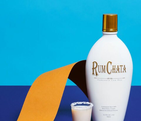 A shooter of salted caramel and a bottle of Rumchata with a golden ribbon and blue background