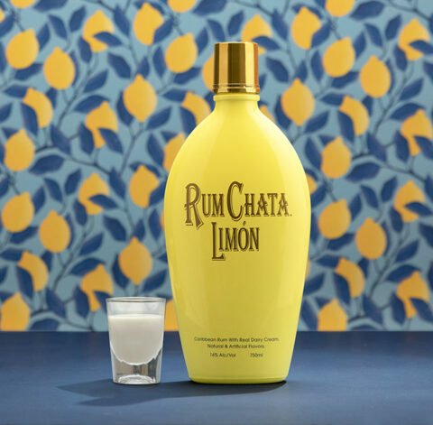 A shot of Rumchata limon and a bottle of Rumchata Limon in front of a blue leaves and lemon wallpaper