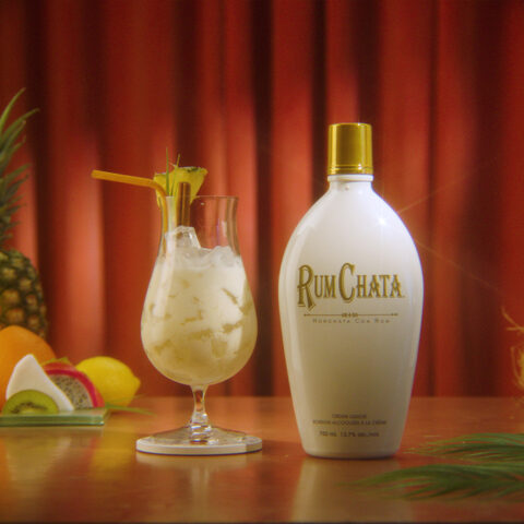 A glass of RumChata Colada beside a Rumchata bottle.